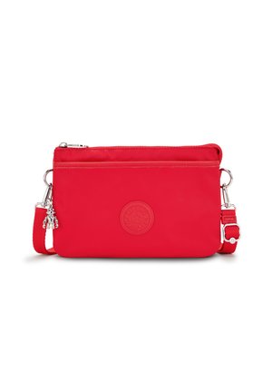 Czerwona nylonowa torba na ramię z teksturowanym okrągłym logo, zamek błyskawiczny i regulowany pasek. Zawiera zawieszkę przymocowaną do boku.