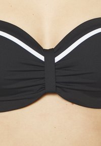 Crni bikini top s bandeau dizajnom, s bijelim detaljima i naboranom teksturom na sredini. Glatka tkanina i zakrivljeni rubovi.