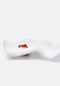 Calcetín de algodón blanco con textura acanalada, que presenta un pequeño diseño bordado en rojo, negro y amarillo en un lado.