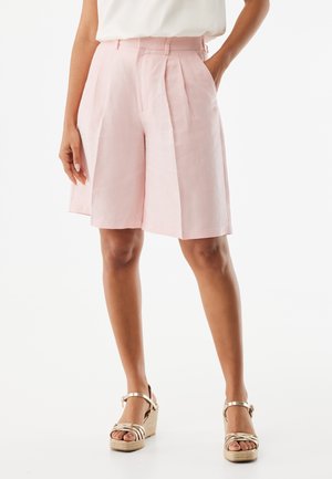 Jasnoróżowe lniane szorty z zakładkami, wysokim stanem i bocznymi kieszeniami. Połączone ze złotymi sandałami na koturnie z paskami.