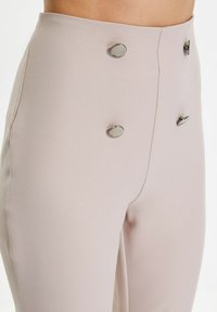 Hoge taille broek van een lichtroze stof met een gladde textuur, voorzien van metalen knopen aan de voorkant voor een extra detail.