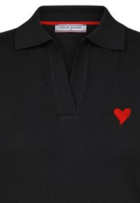 Svart polo shirt med en strukturerad stickad textil, med en röd hjärtbroderi på vänster bröst och en kontrasterande röd inre krage.