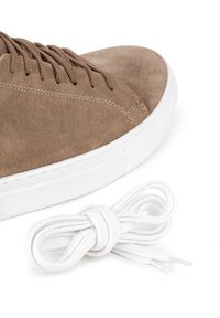 Brązowe zamszowe trampki z białą gumową podeszwą i pasującymi brązowymi sznurowadłami; obok buta są związane dodatkowe białe sznurowadła.