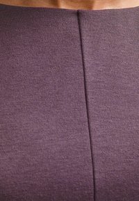 Primer plano de una persona que lleva una prenda de tela púrpura con un detalle de costura vertical cerca del escote.