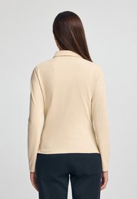 Polo a maniche lunghe beige con colletto, realizzato in un materiale morbido, caratterizzato da una linea dritta e dettagli di cucitura delicati.
