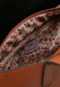 Intérieur d’un sac en cuir marron avec une doublure en tissu fleuri, une poche zippée et une étiquette portant l’inscription "Anna Field."