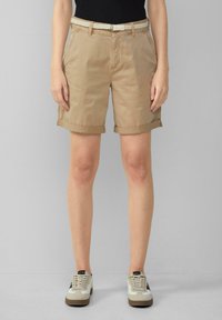 Shorts en coton beige avec des ourlets retroussés, dotés de poches latérales et d'une ceinture tressée blanche. Associés à des sneakers de couleur claire.
