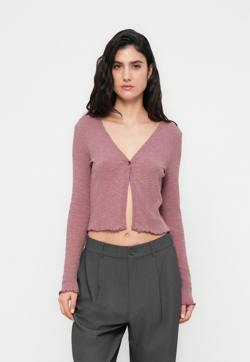 Ριμπ, κοντό, μακρυμάνικο ζακέτα σε μωβ απόχρωση με βαθύ V λαιμόκοψη και κούμπωμα με ένα κουμπί. Διαθέτει ξεφτισμένο τελείωμα και υφασμάτινη υφή.