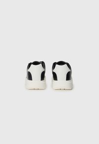 Sneakers din piele alb-negru cu o talpă groasă, având o textură netedă și un design minimalist. Branding Calvin Klein pe călcâi.