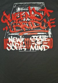 Černé tričko s odvážným textem ve stylu graffiti v červené a bílé barvě. Design obsahuje "QUEENS BRIDGE" a "NEW YORK STATE OF MIND."