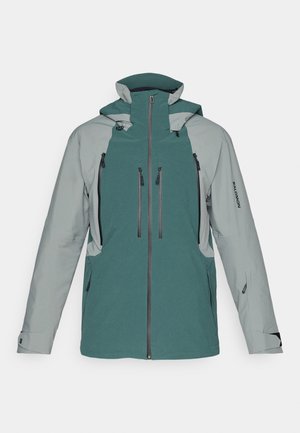 Dvobarvna zelena in siva zunanja jakna z več sprednjimi žepi na zadrgo, nastavljivo kapuco in blagovno znamko na rokavu.