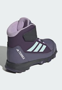 Mid-cut purple boots with black and mint accents. Textured upper, padded collar, and durable sole. Features three stripes logo design.