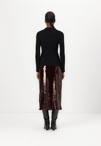Svart ribbad tröja med en åtsittande silhuett, kombinerad med en knälång burgundy paljettkjol. Svarta knähöga klackboots fulländar looken.