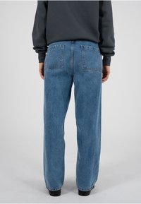 Hellblaue Jeans aus Denim mit weiter Passform, zwei Gesäßtaschen und abgesteppten Nähten. Kombiniert mit einem dunkelgrauen Sweatshirt, von hinten betrachtet.