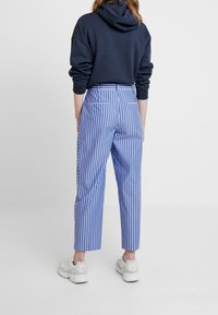 Bawełniana bluza z kapturem w kolorze granatowym, zestawiona z niebieskimi i białymi spodniami w paski, które mają kieszenie boczne i skrócony krój. Uzupełniona białymi sneakerami.