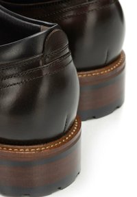 Ciemnobrązowe skórzane buty z zaokrąglonym noskiem i wyściełanym kołnierzem, wyposażone w warstwowy drewniany obcas z ciemnymi paskami i widocznym przeszyciem.