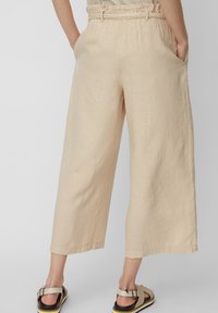Beżowe lniane spodnie o szerokich nogawkach z elastycznym paskiem w talii, z bocznymi kieszeniami, luźnym krojem i długością do kostek.