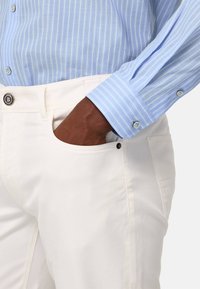 Pantalons blancs avec une poche avant et une fermeture à boutons, associés à une chemise à manches longues rayée bleu clair avec des poignets à boutons.