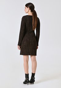 Abito in maglia nera con texture e strisce metalliche, maniche lunghe e gonna svasata; abbinato a stivali alla caviglia neri con dettagli a borchie.