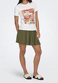 T-shirt blanc avec motif floral, jupe patineuse verte et sandales à motifs noir et blanc. Tissu doux, design décontracté, texture lisse.