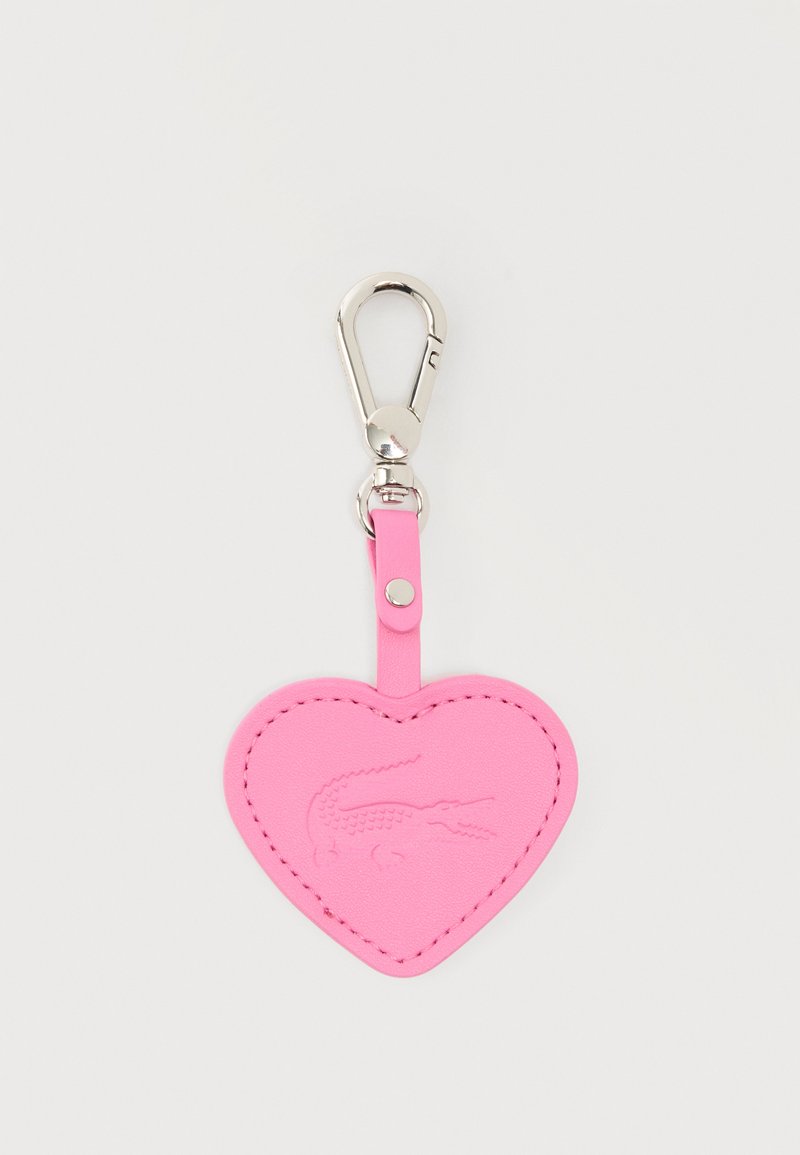 Porte-clés en cuir rose en forme de cœur avec logo crocodile embossé et fermoir en métal argenté sur fond clair.