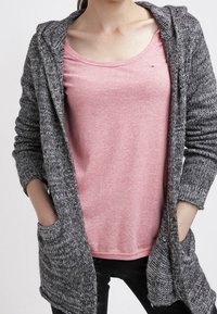 Grå stickad cardigan med huva, med en öppen design fram och fickor, bärs över en ljusrosa t-shirt, med mörka jeans synliga.