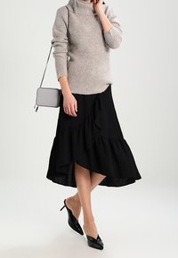 Světlý šedý pletený svetr s vysokým límcem. Volná černá midi sukně s volánky. Černé lodičky s špičatou špičkou. Šedá křížová kabelka.