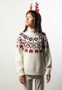 Biały dziergany sweter z czerwonymi i czarnymi kwiatowymi wzorami, z wysokim kołnierzem. Do tego jasne, prążkowane spodnie i czerwone rogi renifera.