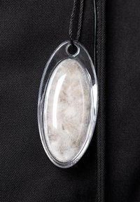 Przezroczysty owalny znacznik z białym, puszystym materiałem w środku, przymocowany do czarnej powierzchni tkaniną cienką czarną nicią.