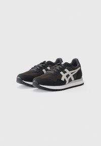 Chaussures de sport noires avec une tige en mesh, accents blancs, semelle en caoutchouc robuste, design à lacets et silhouette classique de course rétro.