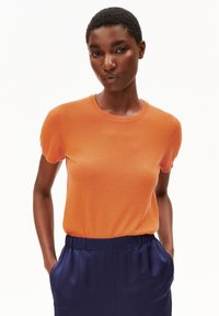 Oranje gebreide top met korte mouwen en een ronde hals, gecombineerd met marineblauwe hoge taillebroeken. Soepele textuur, aansluitend ontwerp.