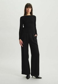 Haut à manches longues noir associé à un pantalon large taille haute noir. Texture lisse, design épuré et style minimaliste dans l'ensemble.