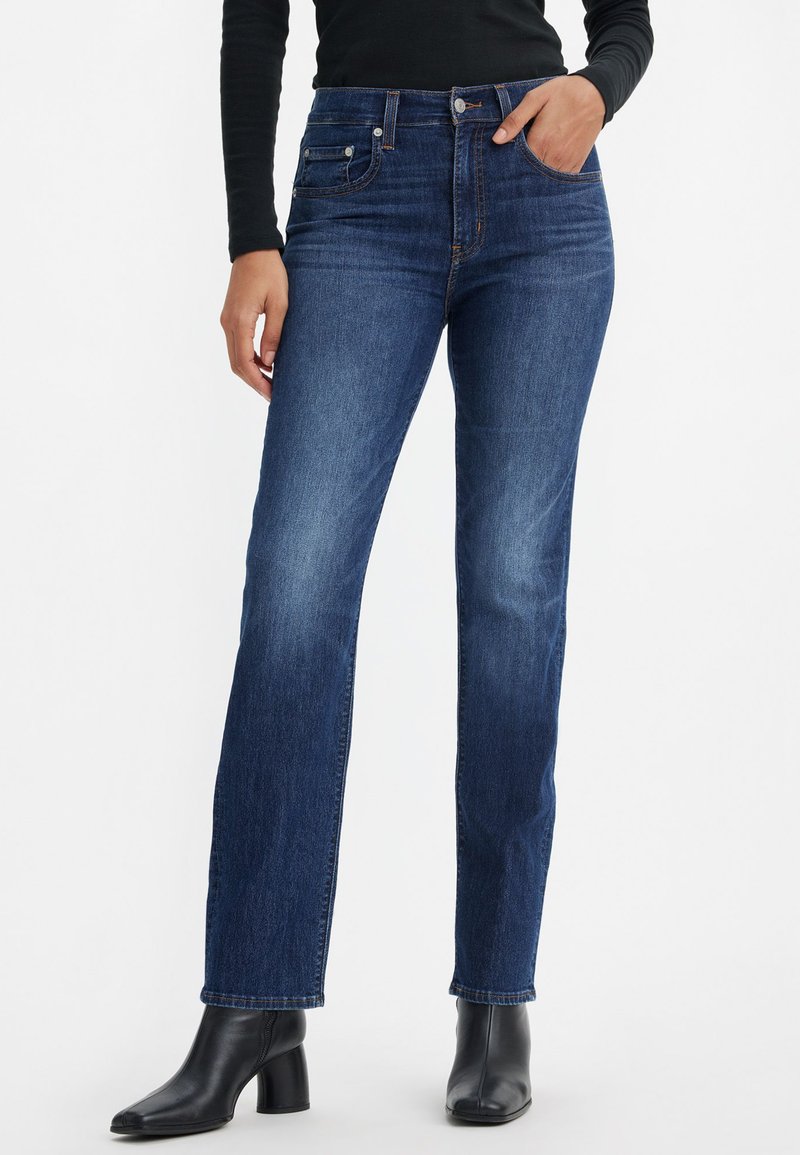 Jeans in denim blu scuro con un design a gamba dritta, dotati di tasche anteriori, vita alta e leggeri sbiadimenti. Abbinati a stivali neri con tacco.