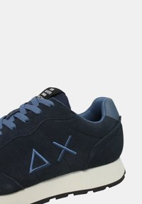 Scarpa da corsa in suede blu scuro con lacci azzurri e suola in gomma. Presenta un logo sul lato e un colletto imbottito per il comfort.