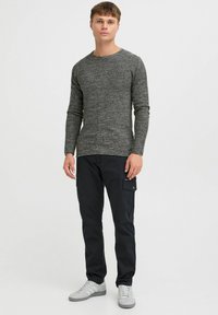 Pulover lung cu textura gri, cu maneci lungi, asortat cu pantaloni cargo negri cu un buzunar lateral. Completat cu teneși gri. Look simplu și funcțional.