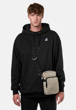 Felpa nera oversize con un piccolo logo, abbinata a una borsa a tracolla beige con zip e tracolla regolabile. Design semplice e funzionale.