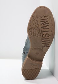 Botín de cuero gris hasta el tobillo con una suela de goma texturizada. Presenta cremalleras decorativas y costuras detalladas. Talla 37 impresa en la suela.