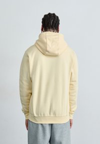 Sweatshirt com capuz amarelo claro, com um corte descontraído, punhos e bainha canelados, combinado com calças de moletom cinzas. Tecido suave e texturizado.