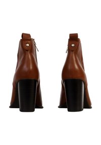 Botas de cuero marrón hasta el tobillo con punta redonda, cremalleras laterales y tacones en bloque de 10 cm. Acentos plateados en el tacón y el tobillo. Textura suave.