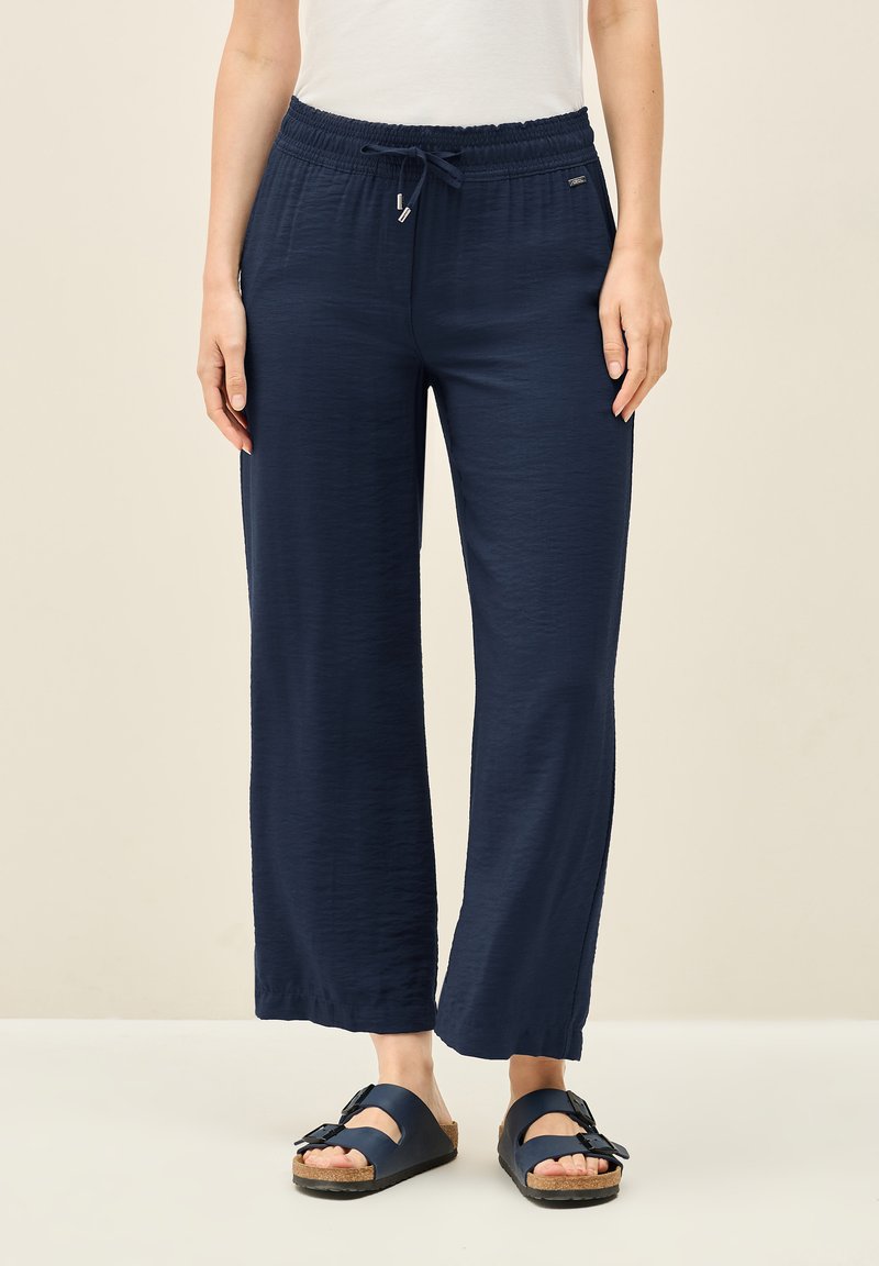 Hose mit weitem Bein in Marineblau, versehen mit einem elastischen Bund und einer Kordel. Weicher, strukturierter Stoff mit relaxtem Schnitt und subtiler glänzender Oberfläche.