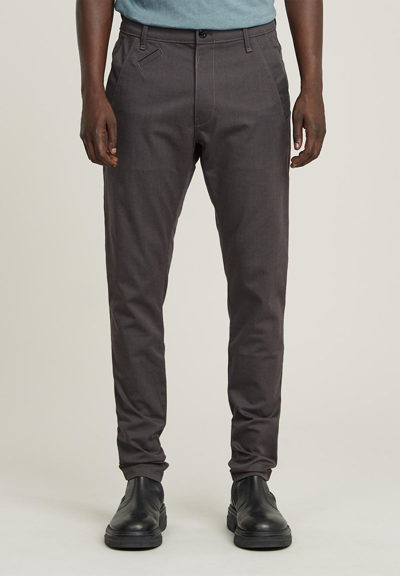 Pantaloni grigi su misura con tasche anteriori, design aderente e texture liscia. Abbinati a stivali neri, con una vita semplice.