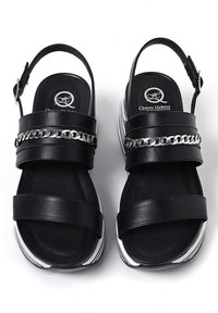 Sandalo nero con una fascia ampia e fibbia regolabile, dotato di un accento a catena metallica sulla parte superiore e di una suola a piattaforma con strisce bianche.