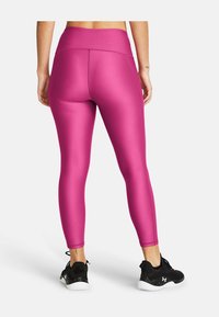 Leggings aderenti a vita alta in tessuto rosa brillante con una texture liscia; indossati con scarpe da ginnastica nere con suola maculata.