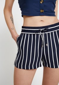 Pantaloni corti a righe blu navy e bianchi con vita elastica, cordoncino e tasche laterali. Tessuto leggero con una consistenza morbida.
