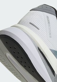 Close-up van de zool en zijkant van een wit-grijze Adidas Adizero Boston 13 hardloopschoen met een gestructureerd mesh bovenwerk en een zwarte rubberen loopzool.