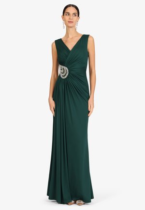 Woman wearing sleeveless dark green floor-length gown with ruched waist and silver jeweled brooch, paired with matching earrings.