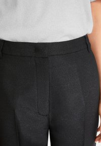 Schwarze Hose aus strukturiertem Stoff mit dezenter glänzender Oberfläche, mit flachem Bund, Gürtelschlaufen und seitlichen Taschen. Minimalistisches Design.