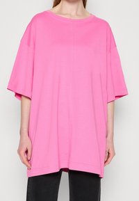 Camiseta rosa de gran tamaño hecha de algodón suave, con mangas cortas, un cuello amplio y un dobladillo recto con costuras mínimas.