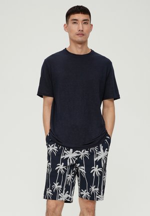 Camiseta de cuello redondo de color marino combinada con pantalones cortos negros con estampado de palmeras blancas. La tela parece ligera; los pantalones cortos tienen bolsillos laterales.