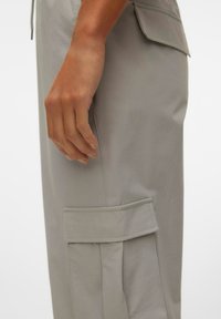 Pantalons cargo gris clair en tissu doux, dotés d'une poche latérale et d'une coupe décontractée. Les coutures visibles ajoutent une texture subtile.